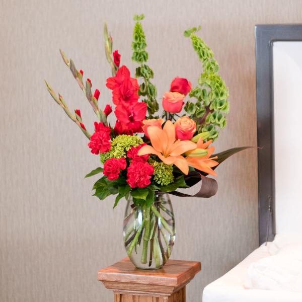 Tall bouquet of orange lilies, red roses, and green blooms in a glass vase