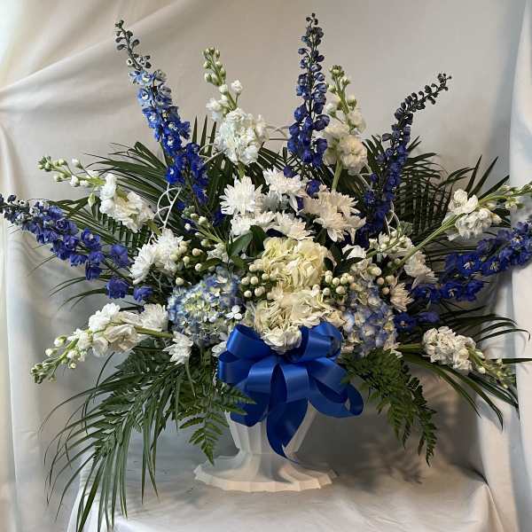 Blue and white floral arrangement in a white pedestal vase with a blue ribbon