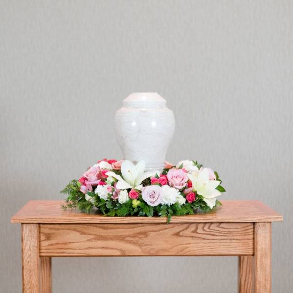 Pink and white floral arrangement around a white urn on a wooden table