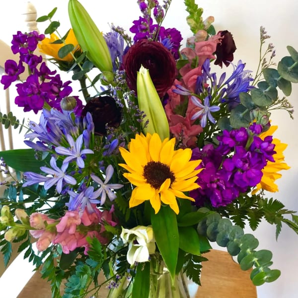 Mixed bouquet with sunflowers, lilies, and purple blooms in a glass vase