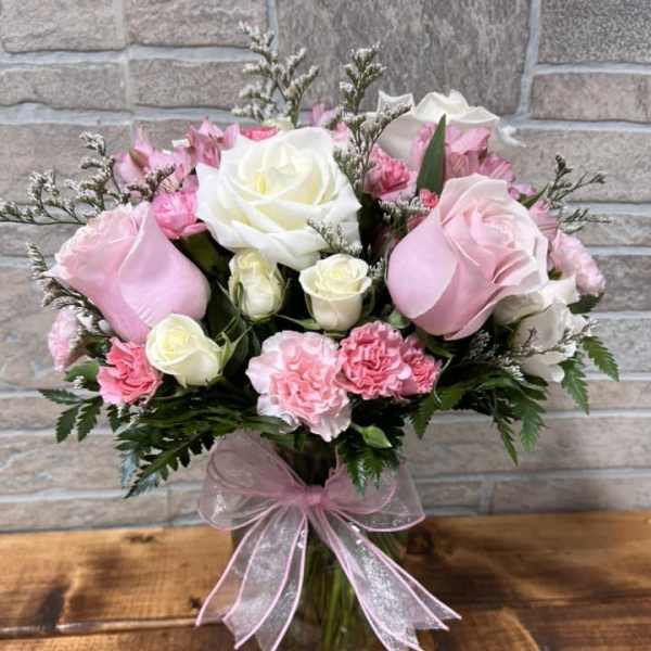 Pink and white roses with pink carnations in a clear glass vase tied with a pink ribbon bow