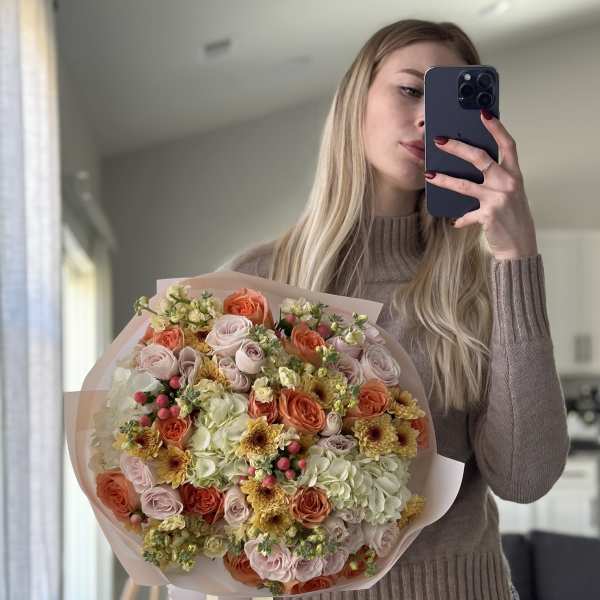 Large bouquet of peach, pink, and cream flowers wrapped in pale paper