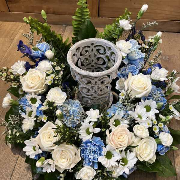 Circular floral wreath with white and blue flowers around a decorative stone urn