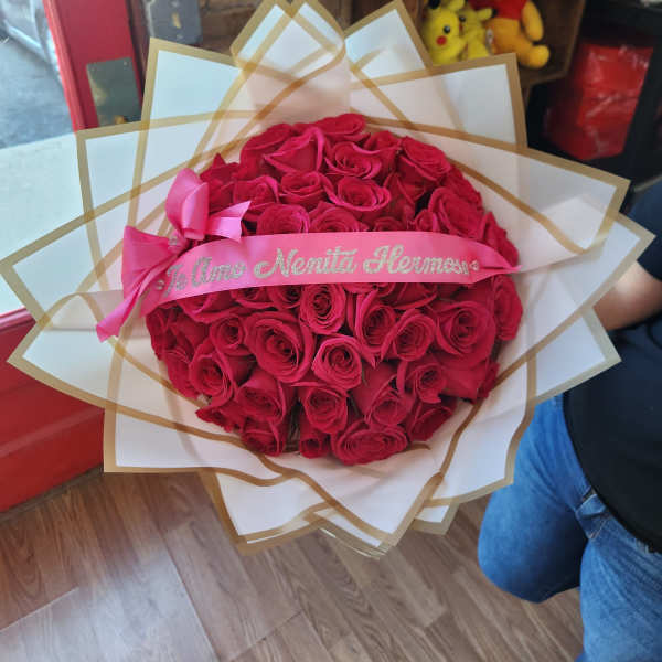 Round bouquet of red roses wrapped in white paper with a pink ribbon