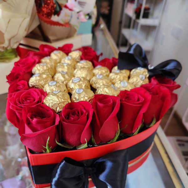 Heart-shaped box of red roses and gold-wrapped chocolates with a black ribbon