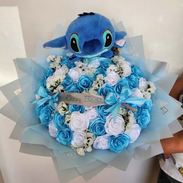 Blue plush toy atop a bouquet of blue and white roses