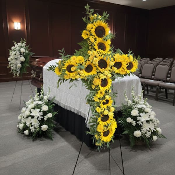 Sunflower funeral spray on a casket with white floral arrangements nearby