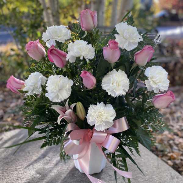 Pink roses and white carnations in a white vase with a pink ribbon