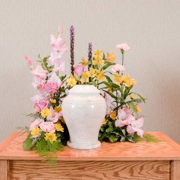 Pink and yellow floral arrangement in a white urn vase