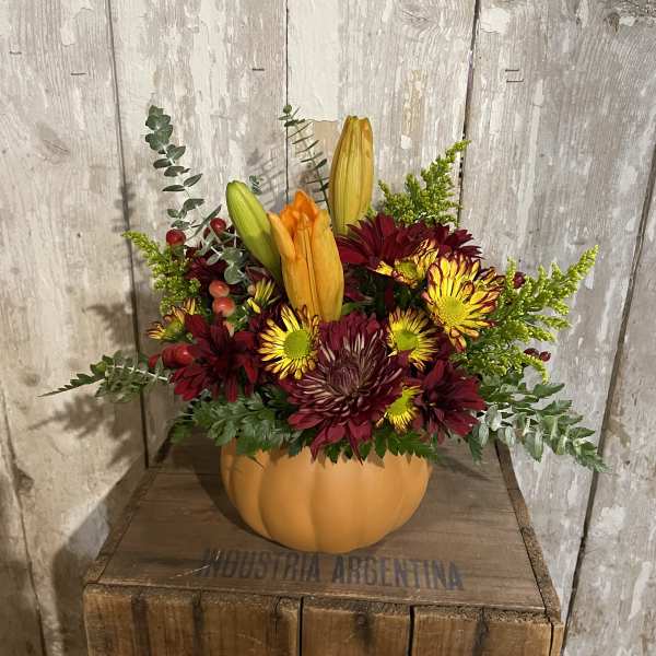 Autumn floral arrangement in a pumpkin-shaped container with lilies and mums