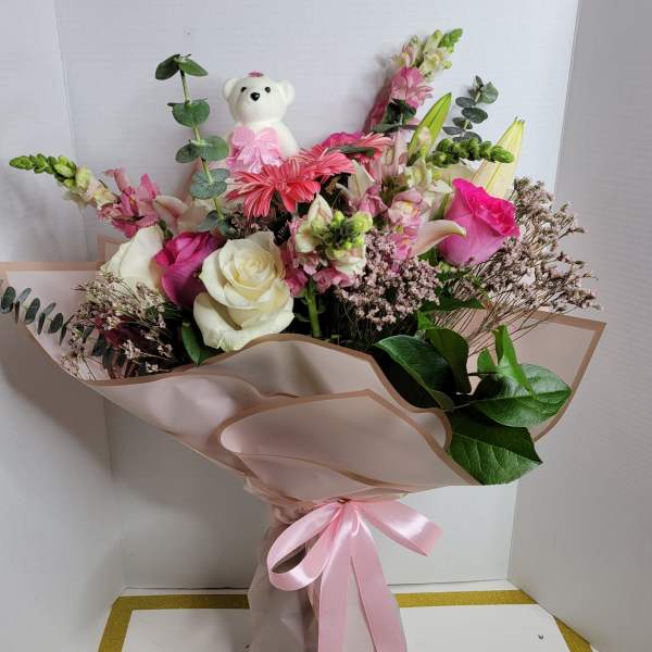 Pink and white bouquet with roses, lilies, and a teddy bear topper