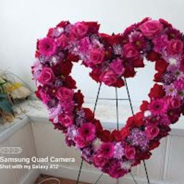Heart-shaped floral wreath of pink and red flowers on a stand