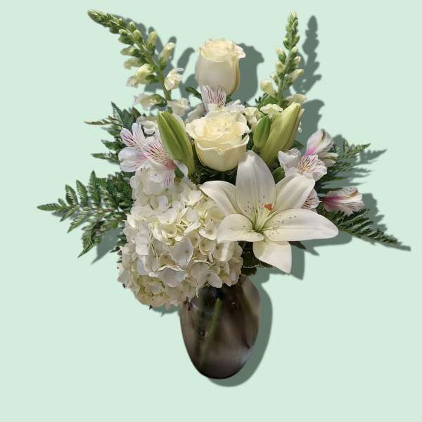 White floral arrangement in a dark vase with lilies and roses