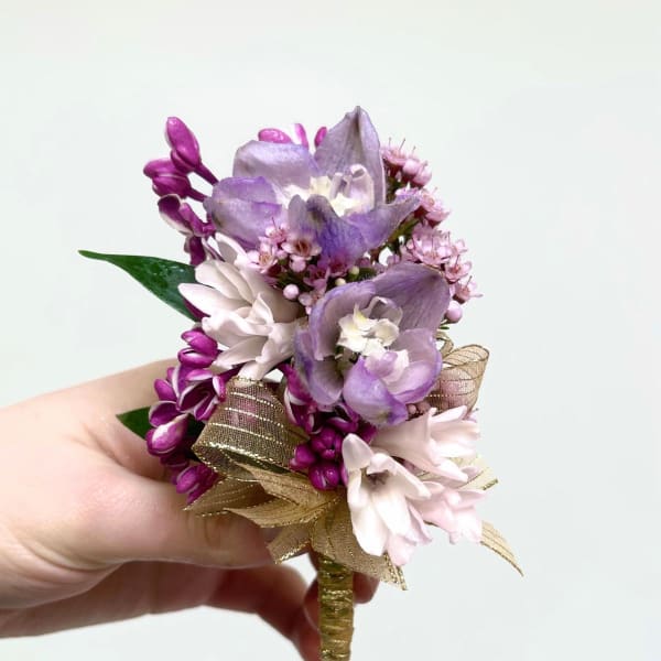 Small handheld boutonniere of purple and pink flowers with a gold ribbon-wrapped stem.
