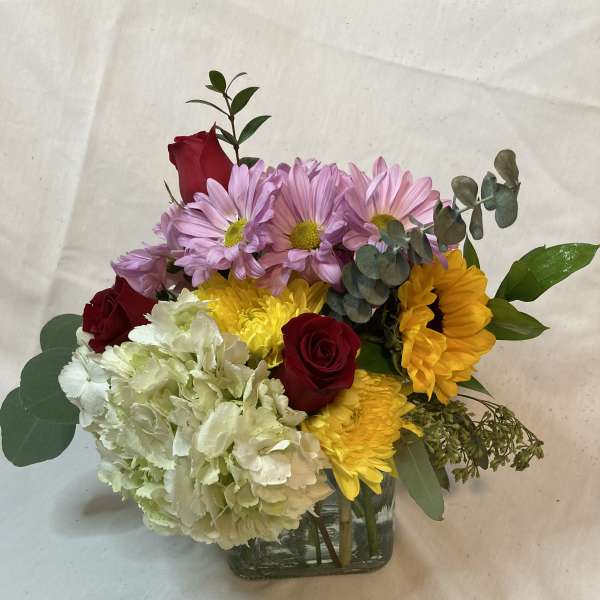 Mixed bouquet of roses, daisies, hydrangea, and sunflowers in a glass vase