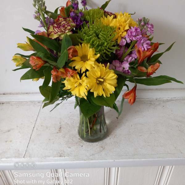 Mixed bouquet of yellow, purple, and orange flowers in a glass vase