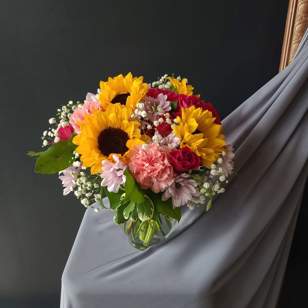 Bouquet of sunflowers, pink roses, and carnations in a glass vase