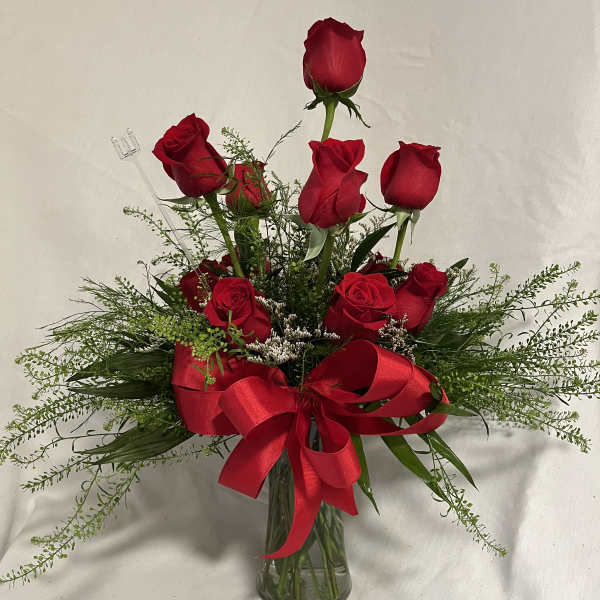 Red roses arranged in a clear glass vase with a large red ribbon