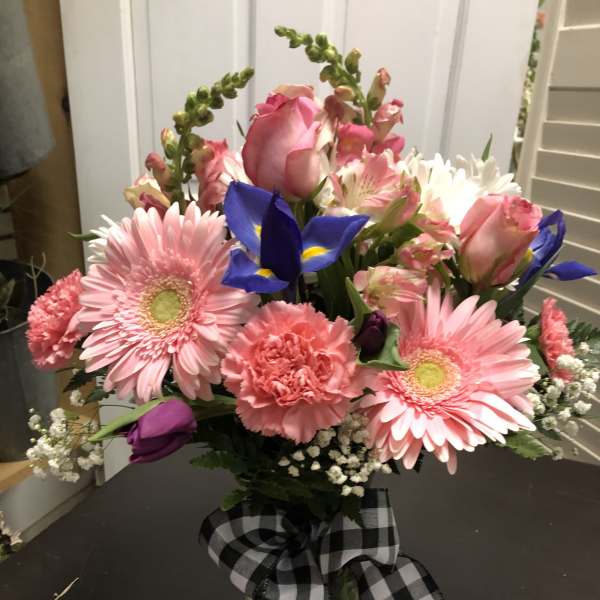 Mixed bouquet of pink gerberas, roses, and blue irises in a glass vase
