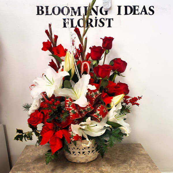 Red roses and white lilies arranged in a basket with holiday ribbon.