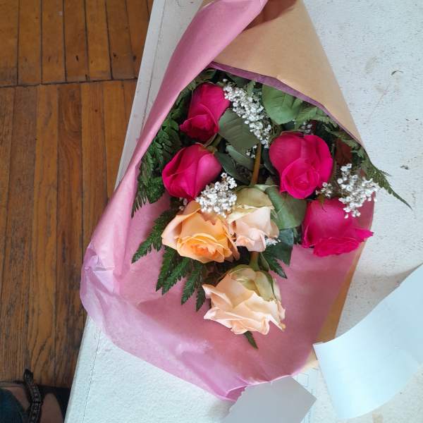 Wrapped bouquet of pink, peach, and cream roses with a red ribbon
