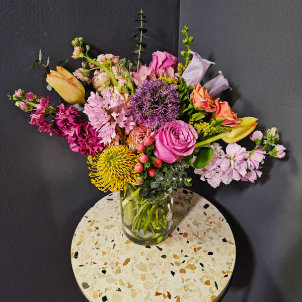 Mixed bouquet of pink, purple, yellow, and peach flowers in a glass vase
