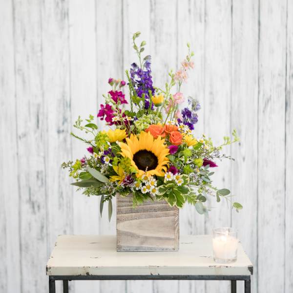 Colorful mixed flower arrangement in a wooden box with a candle beside it