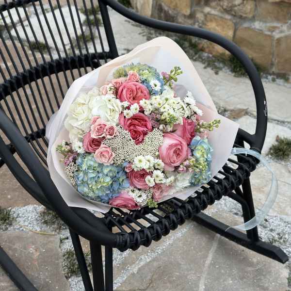 Bouquet of pink and white roses with blue hydrangeas in pale wrapping