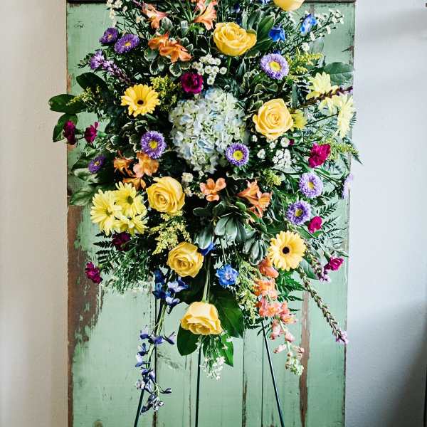 Tall mixed floral spray on a stand with yellow roses and purple blooms