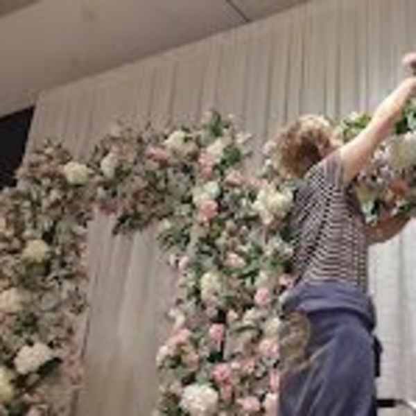 Person arranging a large floral arch with pink and white flowers