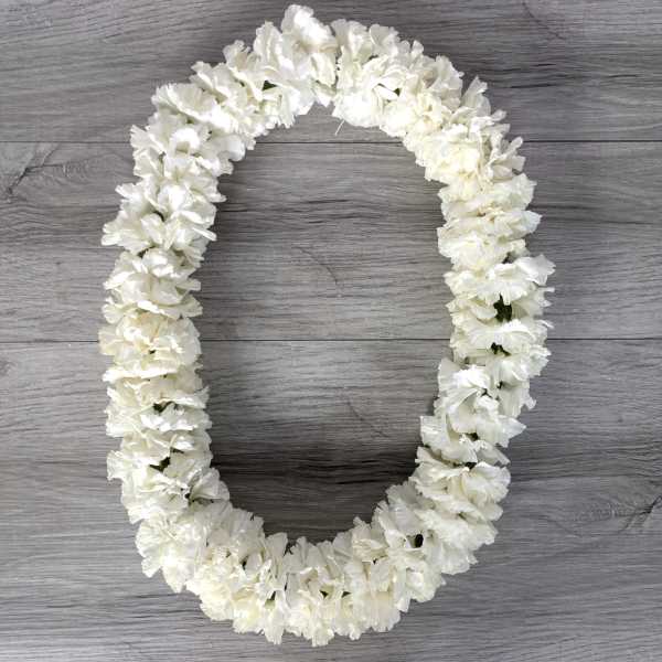White flower lei arranged in an oval shape on a gray wood surface