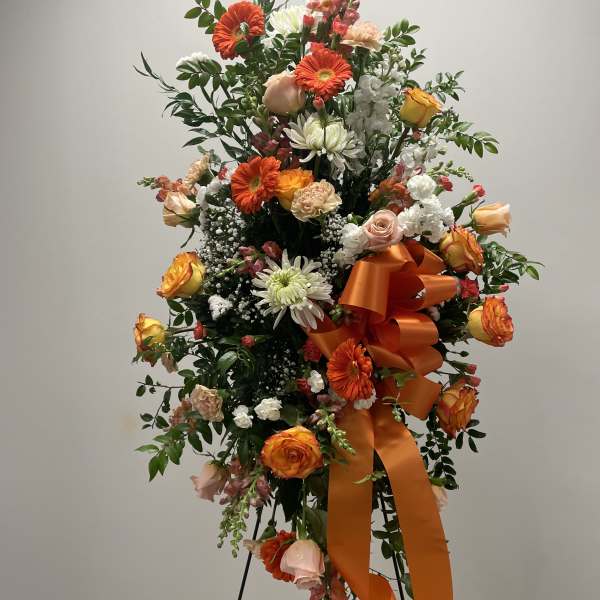 Tall floral standing spray with orange and white flowers and a large orange ribbon