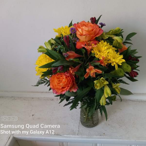 Bouquet of orange roses, yellow chrysanthemums, and mixed blooms in a glass vase