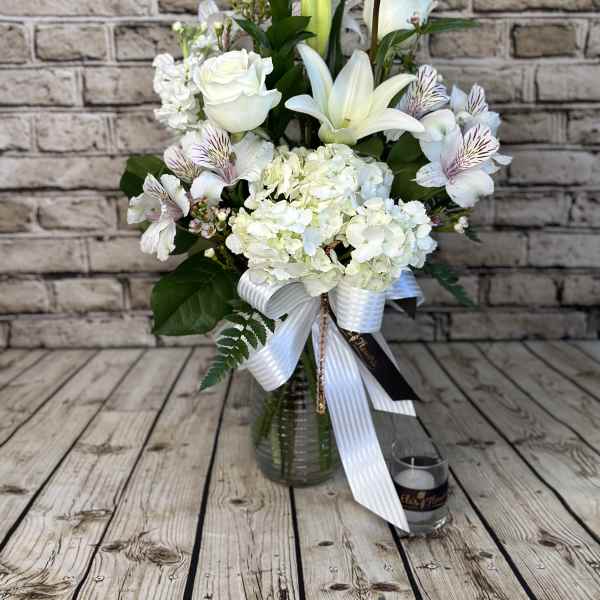 Tall white flower arrangement with lilies, roses, and hydrangeas in a glass vase with a ribbon bow.
