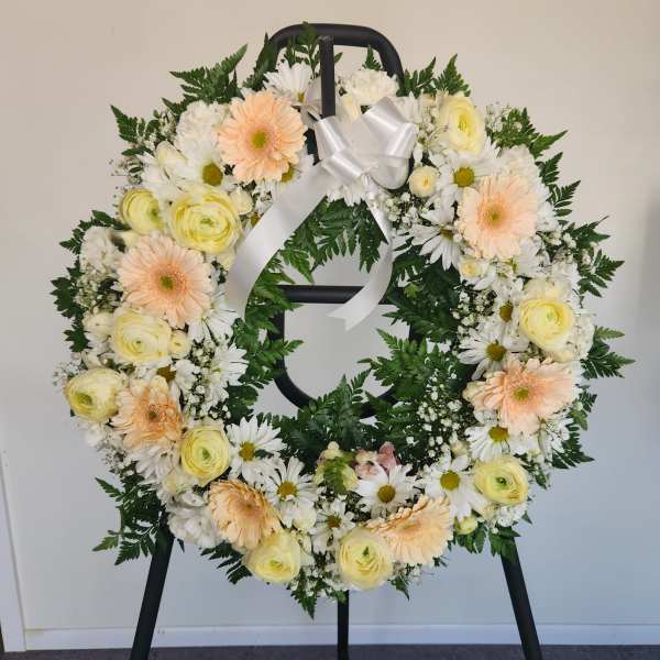 Round floral wreath with white and pale peach flowers on a black stand