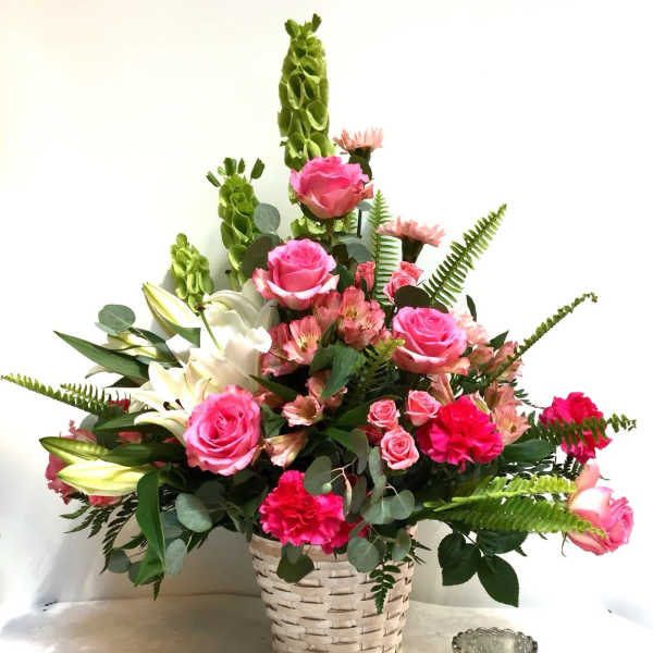Pink roses and lilies arranged in a woven basket with greenery