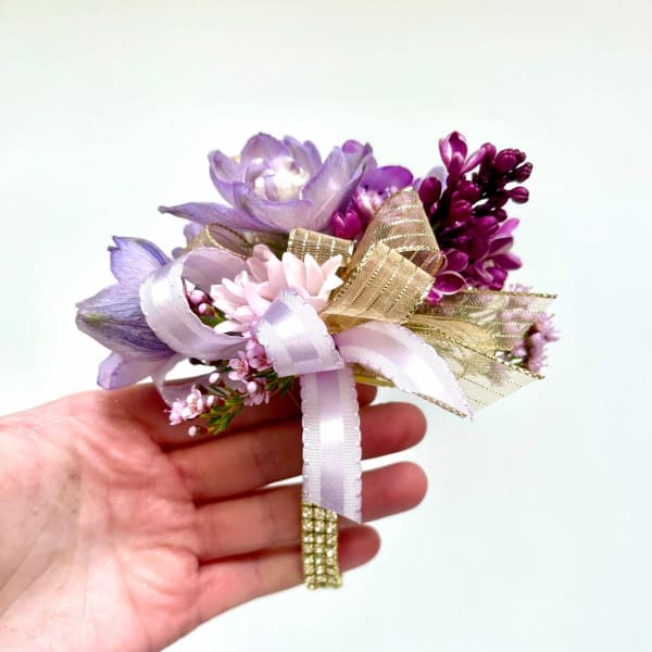 Small handheld corsage of purple and pink flowers with gold and lavender ribbon accents