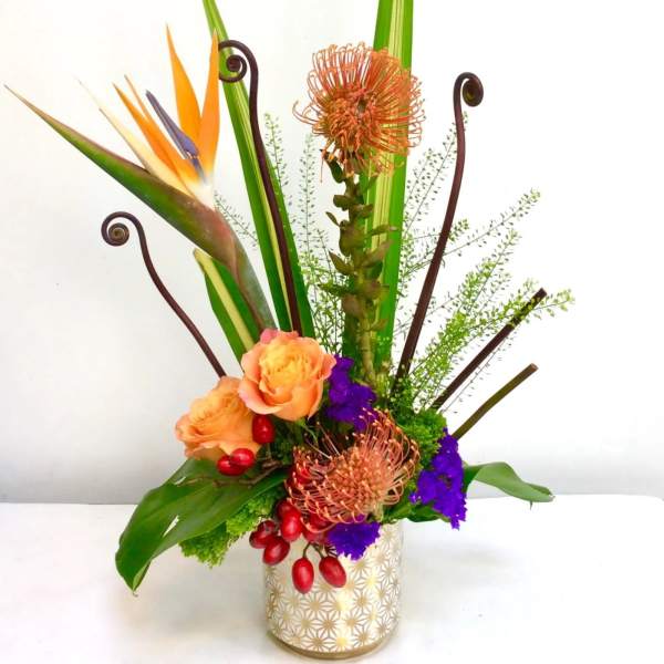 Tall tropical flower arrangement in a patterned vase with orange and purple blooms