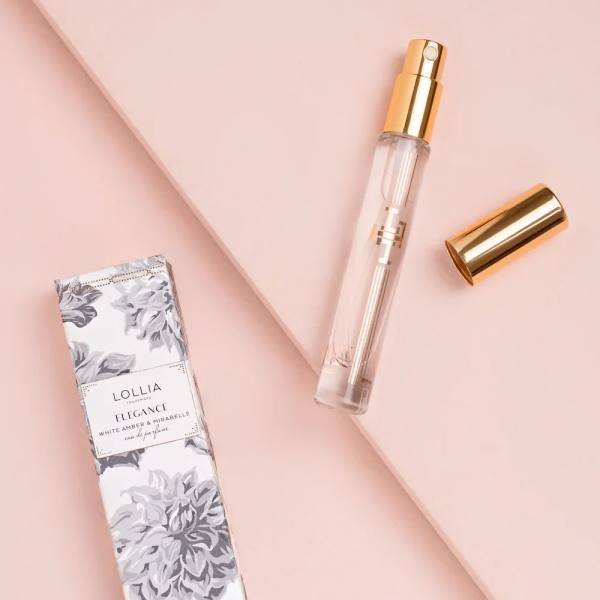 Perfume spray bottle with gold cap and matching box on a pink background