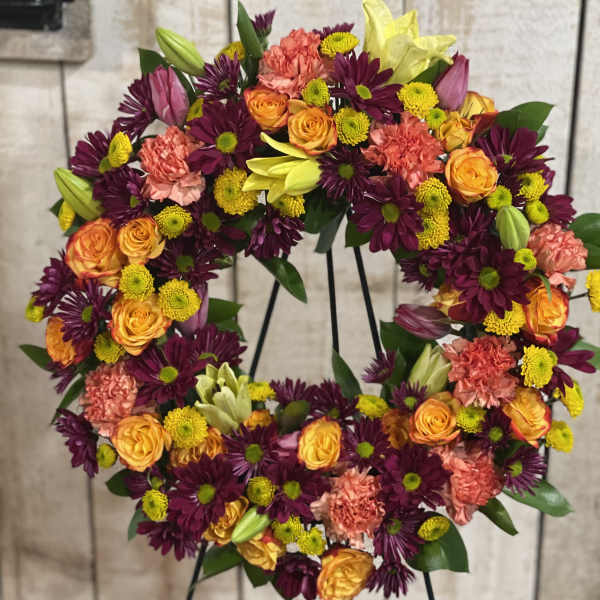 Floral wreath on a stand with orange roses, purple daisies, and pink carnations
