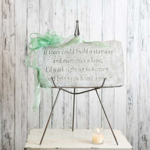 Memorial stone plaque on a metal stand with a green ribbon and candle