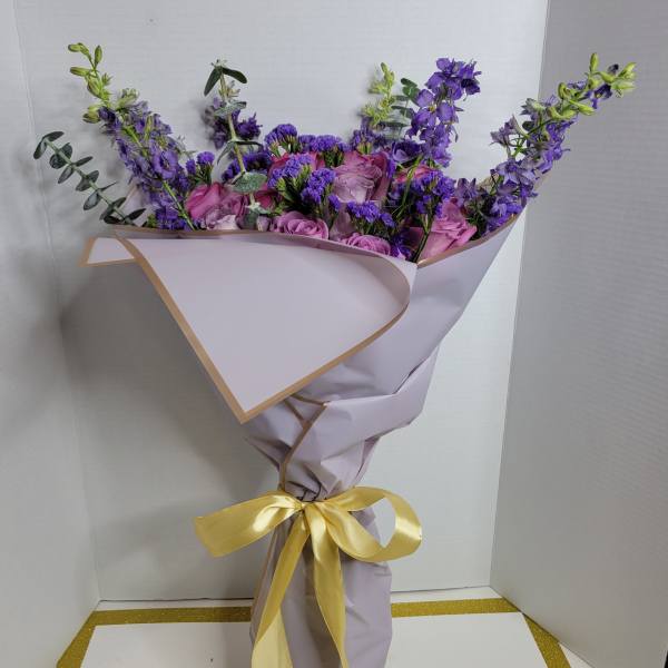 Purple and pink bouquet wrapped in lavender paper with a yellow ribbon