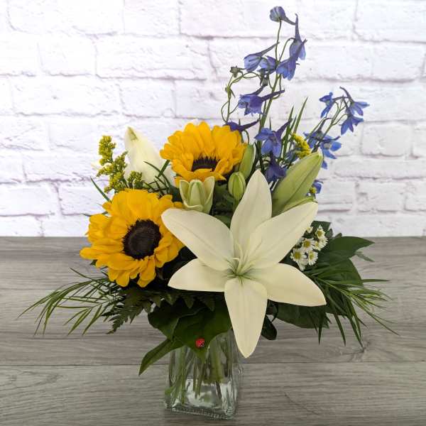 Bouquet of sunflowers, white lilies, and blue delphinium in a glass vase