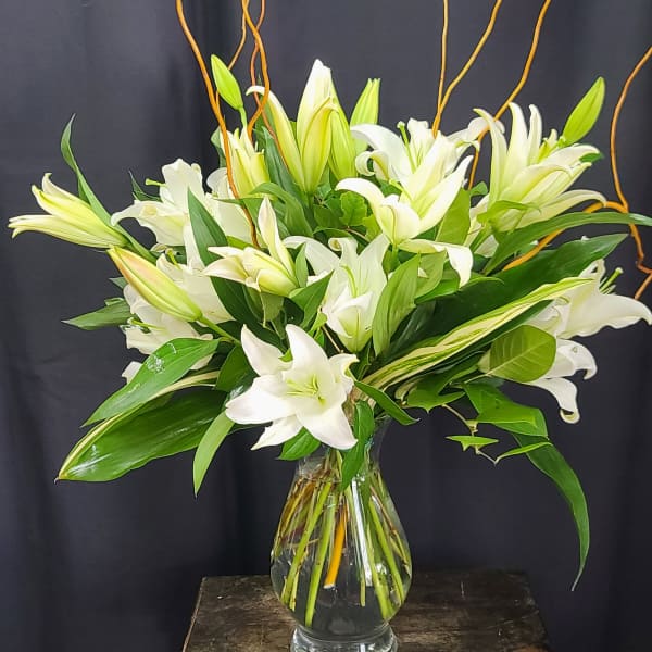 White lilies arranged in a clear glass vase with curly branches