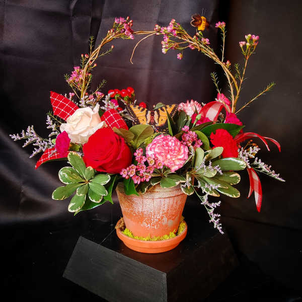 Mixed pink and red floral arrangement in a terracotta pot with a butterfly decoration
