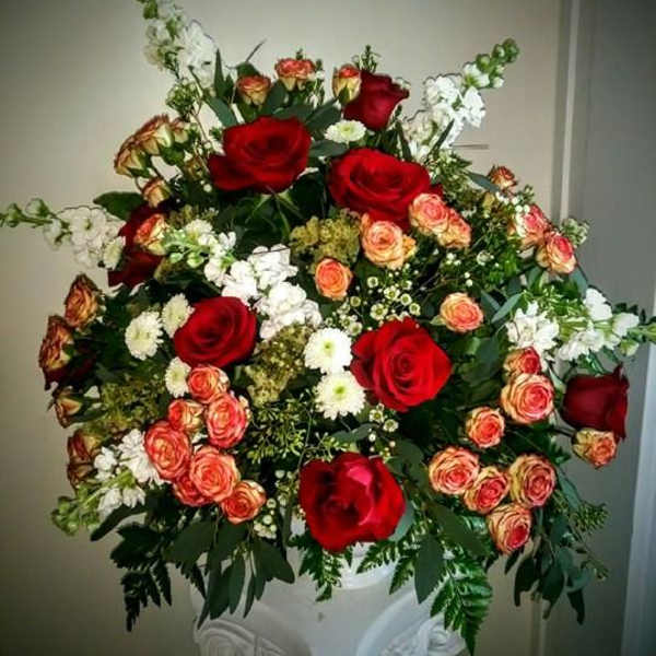 Large bouquet of red and peach roses in a white pedestal vase