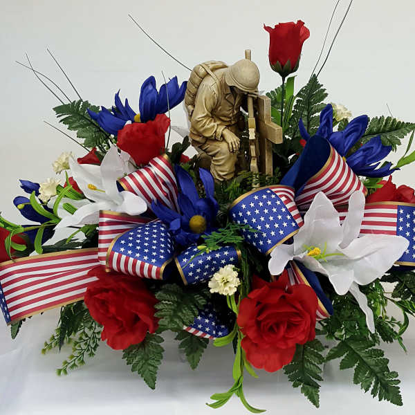 Red, white, and blue floral arrangement with patriotic ribbon and a soldier figurine
