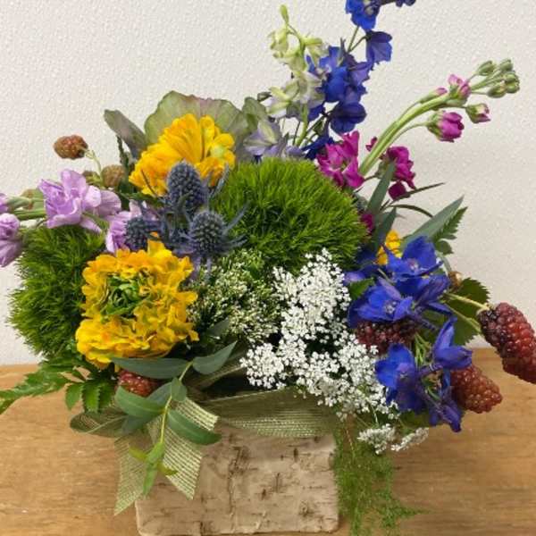 Colorful arrangement of blue, yellow, and purple flowers in a rustic birch container