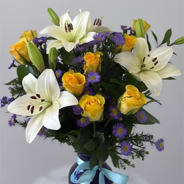 White lilies and yellow roses in a blue vase with a ribbon