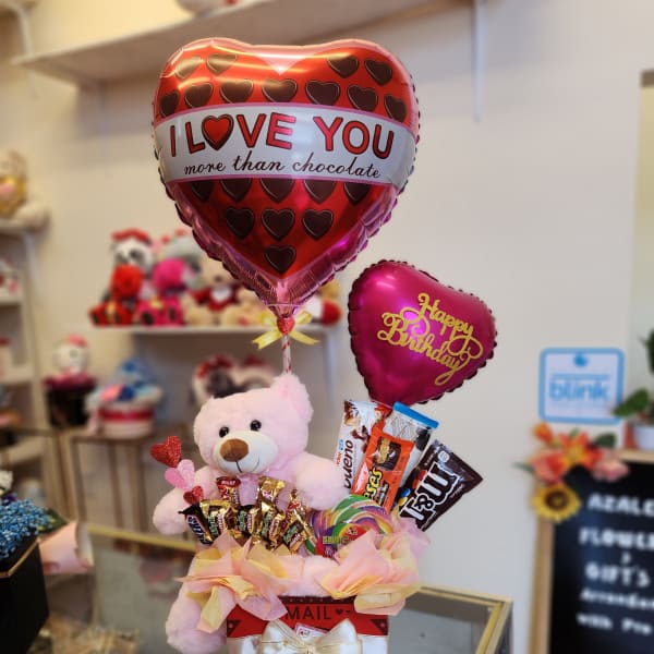Gift arrangement with heart balloons, a teddy bear, and assorted chocolates